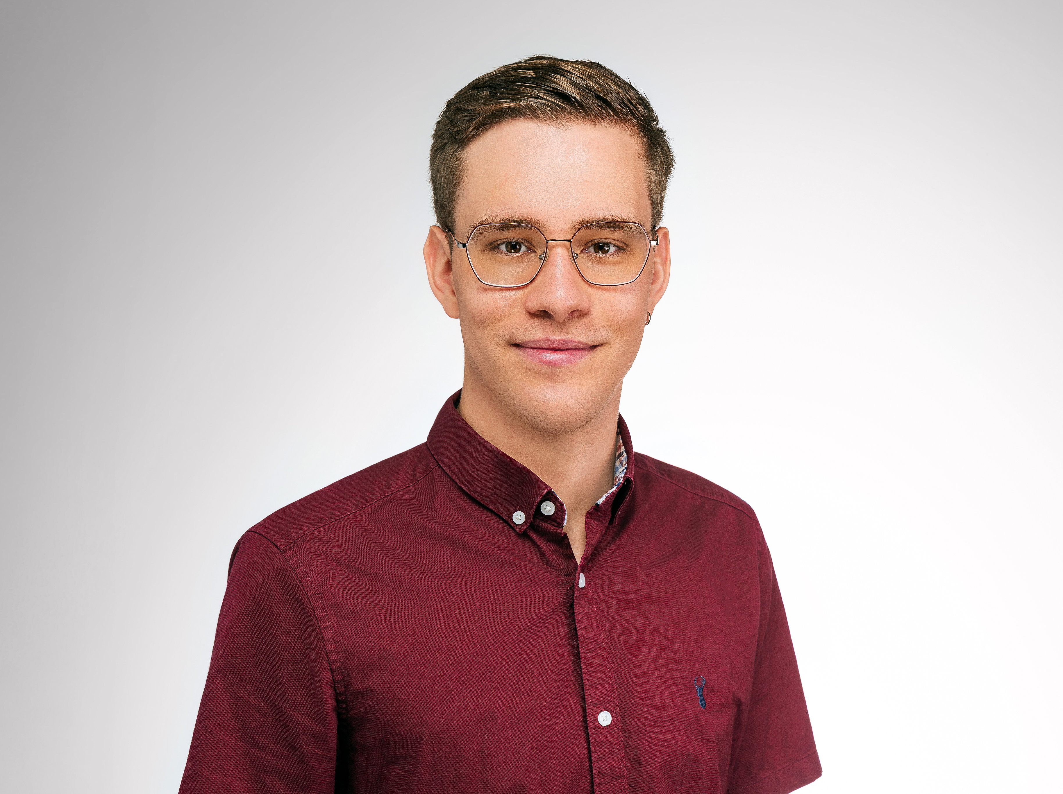 Noah Zimmermann schaut in die Kamera und trägt ein bordeauxrotes Hemd.